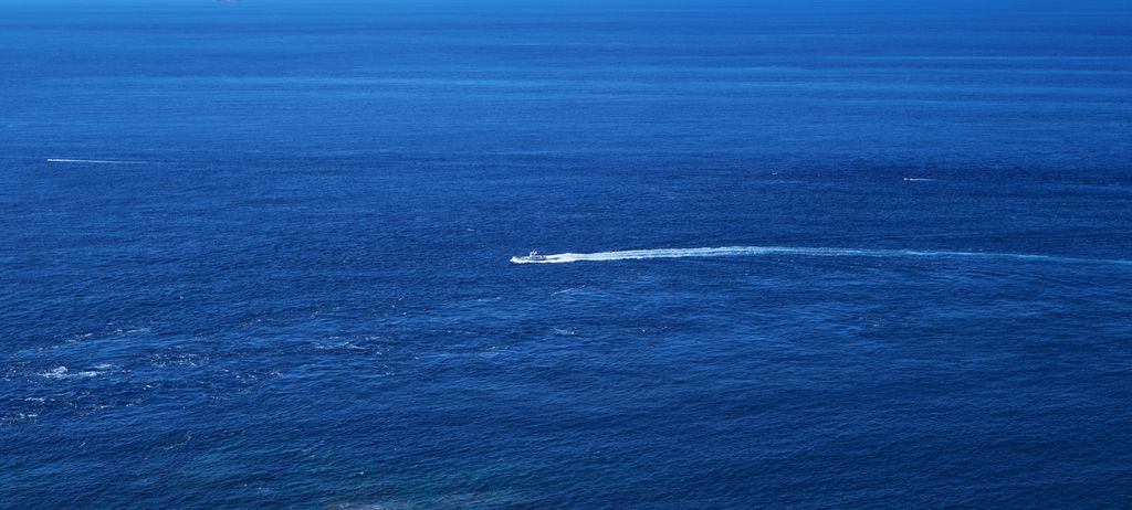 A small boat drawing a white wake across deep blue open sea